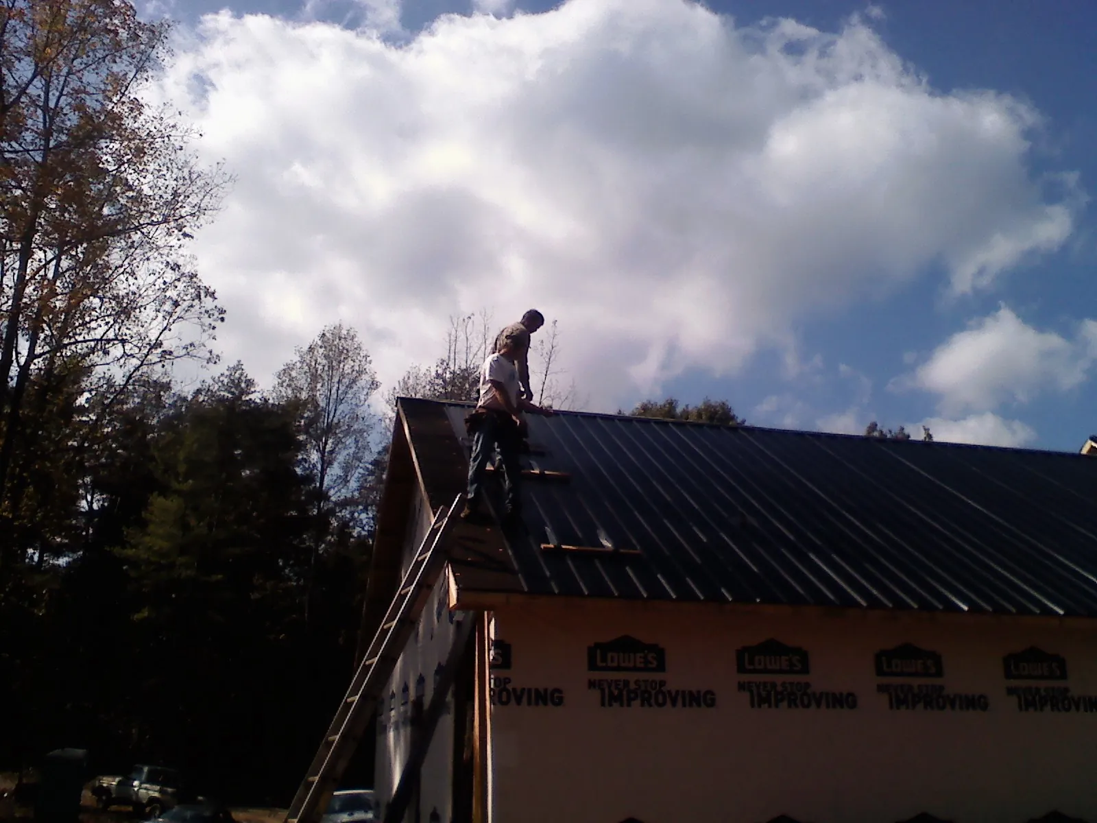 Roofer fastening dark metal panels high against a cloudy sky, from a Roof Inspection job in Tannersville